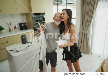 A couple ironing a t-shirt with a steam iron. A couple ironing a t-shirt with a steam iron. 139851982
