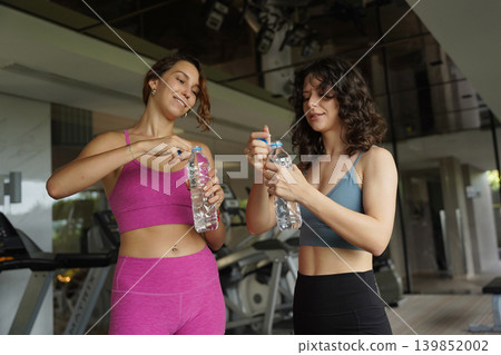 Two women sitting by treadmill hydrating during cooldown 139852002