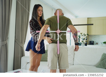 A wife is performing a home physiotherapy program on her husband to correct his posture A wife is performing a home physiotherapy program on her husband to correct his posture 139852232