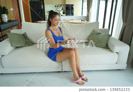 A woman in blue athletic wear doing resistance band exercise indoors 139852233