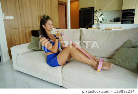 A woman in blue athletic wear doing resistance band exercise indoors A woman in blue athletic wear doing resistance band exercise indoors 139852234