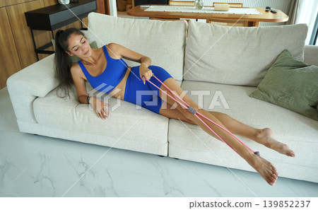 A woman in blue athletic wear doing resistance band exercise indoors A woman in blue athletic wear doing resistance band exercise indoors 139852237
