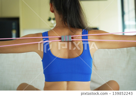A woman in blue athletic wear doing resistance band exercise indoors A woman in blue athletic wear doing resistance band exercise indoors 139852243