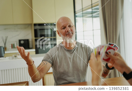 A man and a woman play cards at a wooden table in a sunlit modern living room A man and a woman play cards at a wooden table in a sunlit modern living room 139852381