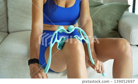 A woman in blue workout clothes uses a turquoise roller to thigh A woman in blue workout clothes uses a turquoise roller to thigh 139852697