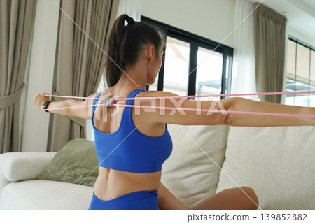 A woman in blue athletic wear doing resistance band exercise indoors A woman in blue athletic wear doing resistance band exercise indoors 139852882
