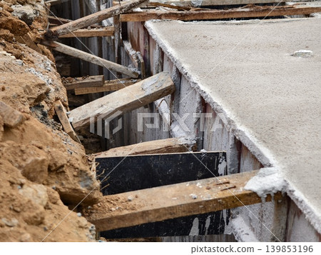 Narrow ditch with reinforcement, waterproof concrete trench bounded by soil and support stakes Narrow ditch with reinforcement, waterproof concrete trench bounded by soil and support stakes 139853196