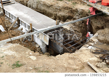 Narrow ditch with reinforcement, waterproof concrete trench bounded by soil and support stakes Narrow ditch with reinforcement, waterproof concrete trench bounded by soil and support stakes 139853215