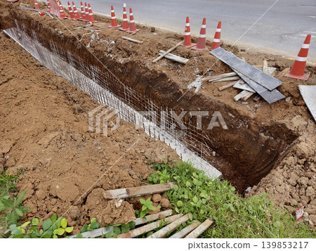 Narrow ditch with reinforcement, waterproof concrete trench bounded by soil and support stakes Narrow ditch with reinforcement, waterproof concrete trench bounded by soil and support stakes 139853217