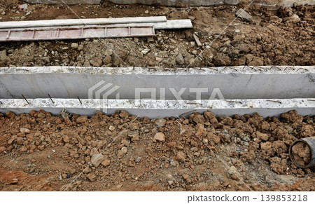 Narrow ditch with reinforcement, waterproof concrete trench bounded by soil and support stakes Narrow ditch with reinforcement, waterproof concrete trench bounded by soil and support stakes 139853218