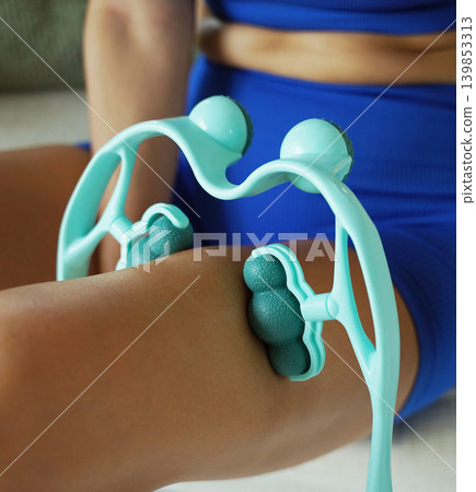A woman in blue workout clothes uses a turquoise roller to thigh 139853313
