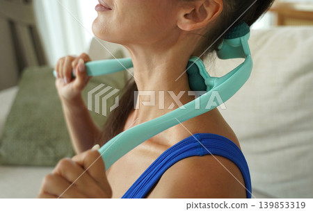 A woman uses a turquoise neck massager after a workout A woman uses a turquoise neck massager after a workout 139853319