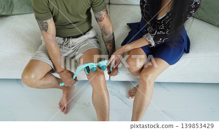 A woman helps a man use a massage roller to rehabilitate his knee A woman helps a man use a massage roller to rehabilitate his knee 139853429