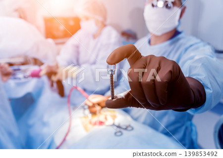 Spinal surgery. Surgeon show polyaxial screw in operating room Spinal surgery. Surgeon show polyaxial screw in operating room 139853492