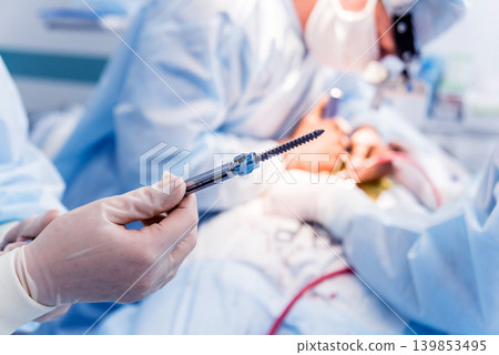 Spinal surgery. Surgeon show polyaxial screw in operating room Spinal surgery. Surgeon show polyaxial screw in operating room 139853495