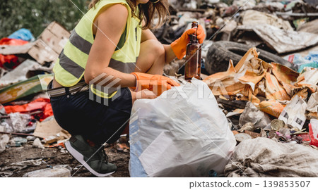 Woman volunteer helps clean the field of plastic garbage. Woman volunteer helps clean the field of plastic garbage. 139853507