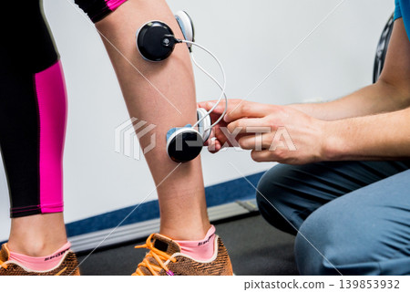 Physical therapist install electrostimulator on the muscles of the legs. Physical therapist install electrostimulator on the muscles of the legs. 139853932