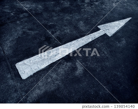 White arrow painted on rough asphalt, centered in frame with high contrast grainy texture. 139854140