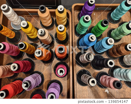 Colorful sewing thread spools arranged in wooden tray with shallow depth of field, glossy Colorful sewing thread spools arranged in wooden tray with shallow depth of field, glossy 139854147