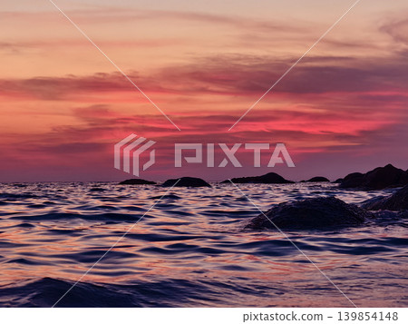 Vibrant sunset over rocky coastal waves, pink and coral sky reflecting on rippling ocean surface. Vibrant sunset over rocky coastal waves, pink and coral sky reflecting on rippling ocean surface. 139854148