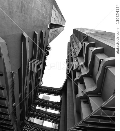 Concrete balconies rising in stark geometry, towering facade with deep shadows and rough texture Concrete balconies rising in stark geometry, towering facade with deep shadows and rough texture 139854154