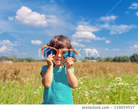 Happy little girl looking through big sunglasses Happy little girl looking through big sunglasses 139854557