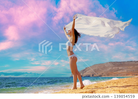 Young woman with a fluttering pareo in her hands on the beach Young woman with a fluttering pareo in her hands on the beach 139854559