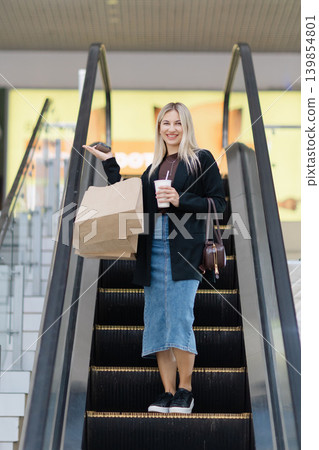 Smiling woman holding shopping bags on escalator lifestyle Smiling woman holding shopping bags on escalator lifestyle 139854801