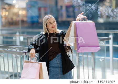 Woman smiling and holding many shopping bags in mall Woman smiling and holding many shopping bags in mall 139854807