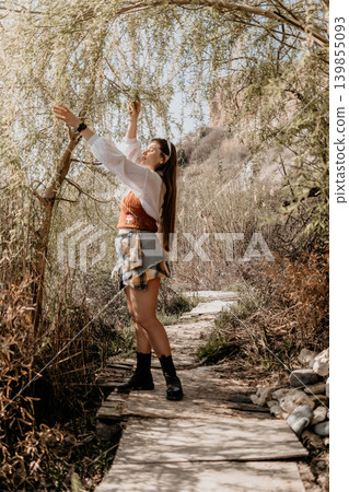 Woman willow nature young woman stands on a wooden path reaching for tree branches in a sunny park landscape Woman willow nature young woman stands on a wooden path reaching for tree branches in a sunny park landscape 139855093