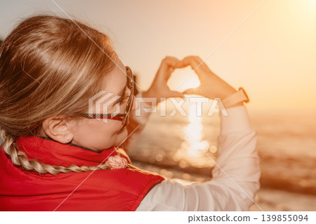 Heart sunset woman framing the golden sun with her hands over the ocean waves during a romantic evening at the beach Heart sunset woman framing the golden sun with her hands over the ocean waves during a romantic evening at the beach 139855094