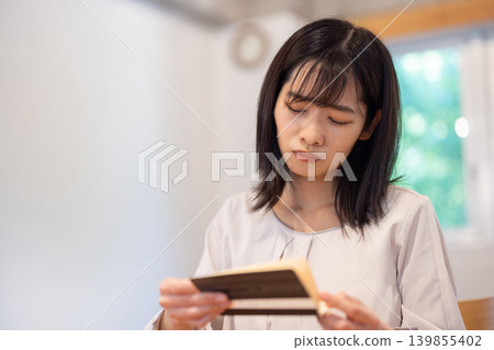 A young Japanese woman frowns as she looks at her bankbook. A young Japanese woman frowns as she looks at her bankbook. 139855402