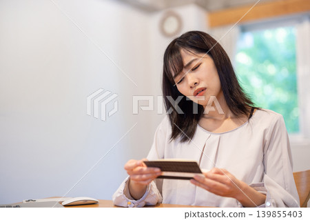 A young Japanese woman frowns as she looks at her bankbook. A young Japanese woman frowns as she looks at her bankbook. 139855403