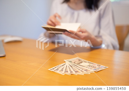 A woman's hands flipping through a 10,000 yen bill and a bankbook on a table. A woman's hands flipping through a 10,000 yen bill and a bankbook on a table. 139855450