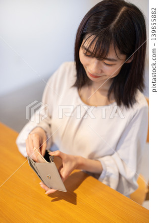 A close-up of a woman's hands as she takes banknotes out of her wallet at a table. A close-up of a woman's hands as she takes banknotes out of her wallet at a table. 139855882