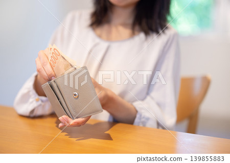 A close-up of a woman's hands as she takes banknotes out of her wallet at a table. A close-up of a woman's hands as she takes banknotes out of her wallet at a table. 139855883
