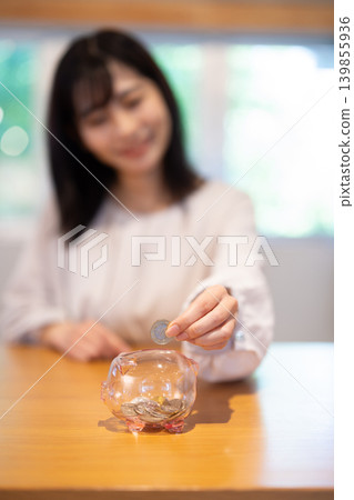 特寫鏡頭拍攝一位女士將硬幣放入存錢筒的手。 139855936