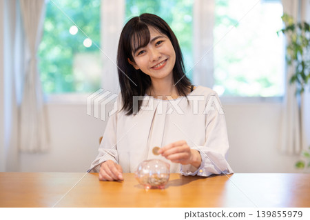 一位年輕的日本女子麵帶微笑地往存錢筒裡放硬幣。 139855979
