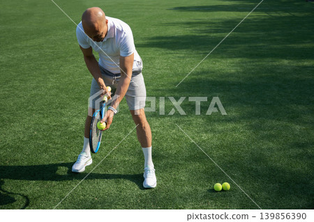 Athletic mature tennis player standing with racket and ball outdoors Athletic mature tennis player standing with racket and ball outdoors 139856390