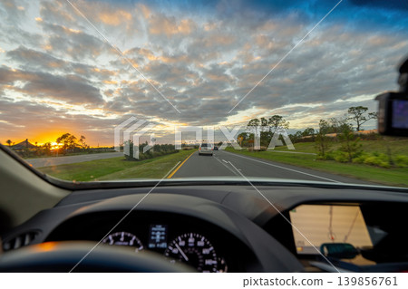 POV commute through rural town district, dashboard visible, cars merging at intersection, street lights turning on as evening approaches. POV commute through rural town district, dashboard visible, cars merging at intersection, street lights turning on as evening approaches. 139856761
