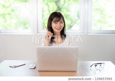 一位年輕的日本女子麵帶微笑，在電腦前舉起食指。 139857093