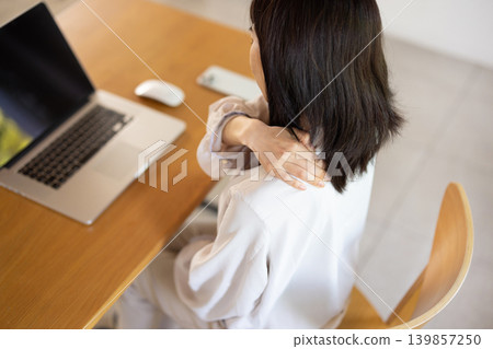 A young Japanese woman with her hand on her shoulder and frowning while working on her computer. 139857250