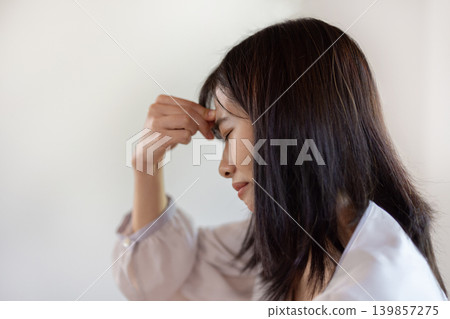 A young Japanese woman puts her hand to her head and frowns while working on her computer. A young Japanese woman puts her hand to her head and frowns while working on her computer. 139857275