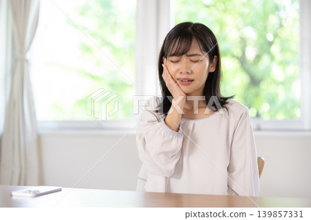 一位年輕的日本女子摀著臉頰，臉上露出痛苦的表情。 139857331
