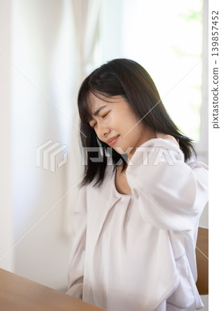 A young Japanese woman with her hand on her shoulder and a frown on her face. A young Japanese woman with her hand on her shoulder and a frown on her face. 139857452