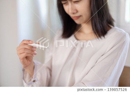 A young Japanese woman in her living room looks distressed while looking at a thermometer. A young Japanese woman in her living room looks distressed while looking at a thermometer. 139857526