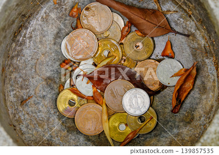 An overhead view of Japanese coins and fallen leaves collected in the purification fountain and offering box of a Shinto shrine. An overhead view of Japanese coins and fallen leaves collected in the purification fountain and offering box of a Shinto shrine. 139857535