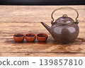 Vintage ceramic teapot with brass handle and three small clay tea cups filled with dark tea on wood 139857810