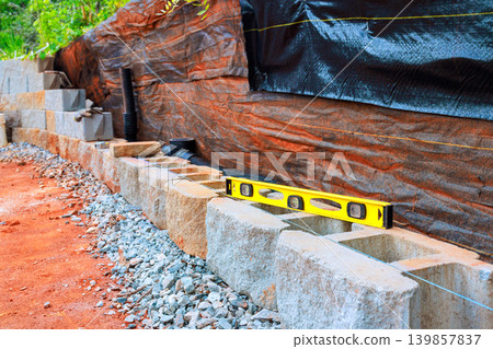 Workers are building retaining stone wall using concrete blocks checking level of structure with tool. Workers are building retaining stone wall using concrete blocks checking level of structure with tool. 139857837