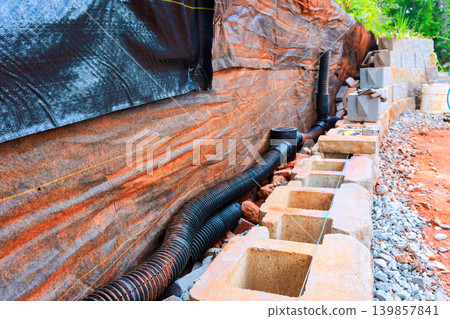 Workers are setting up drainage system using pipes, concrete blocks along site with retaining wall Workers are setting up drainage system using pipes, concrete blocks along site with retaining wall 139857841
